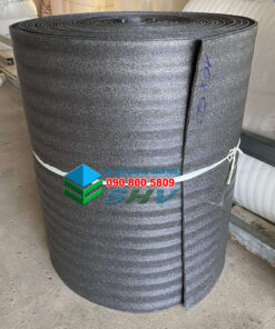 Cuộn vật liệu cách âm, cách nhiệt màu xám đen, được quấn tròn và buộc chặt, đặt trong kho hàng.