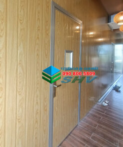 Tường được ốp bằng tấm vật liệu giả gỗ màu nâu nhạt, có khung viền màu xám, trong không gian nội thất.
