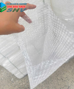 Một tay cầm tấm bong bóng nhựa trong suốt, đặt trên mặt bàn đá hoa.