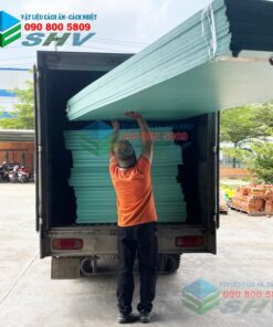 Người công nhân đang bốc dỡ tấm panel cách âm màu xanh lam vào thùng xe tải.